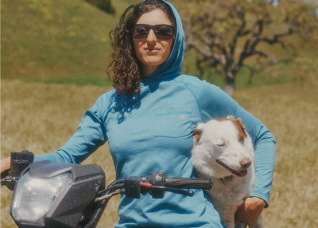 Woman holding a dog, leaning agasint a scooter wearing a temp Iq hoodie