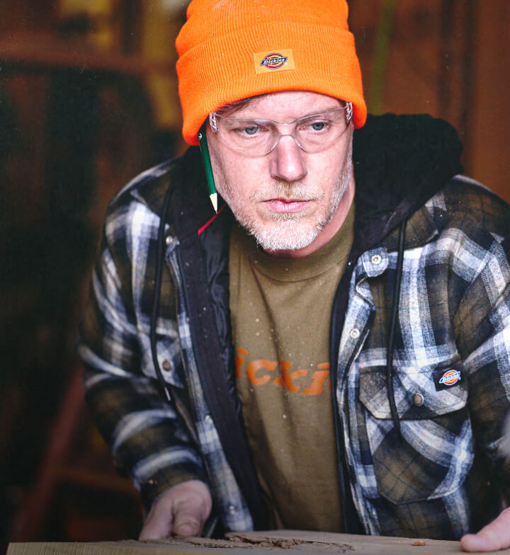 A man wearing an orange dickies head covering while squaring up a piece of work material.