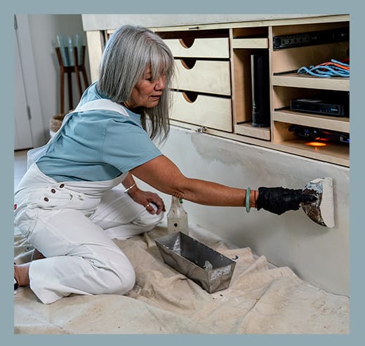 A woman kneeling on the ground applying texture to a wall