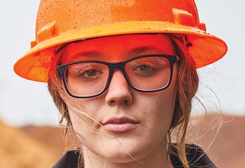 close up image of a young woman wearing glasses and an orange hardhat