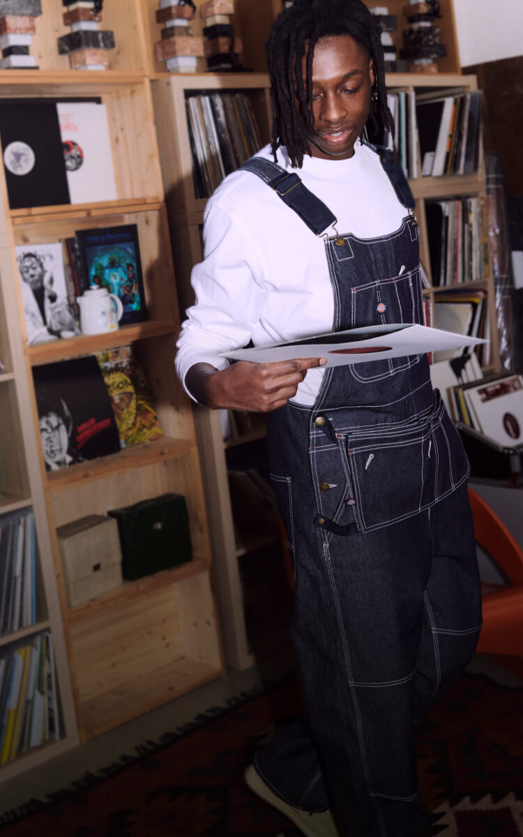 A person wearing dickies bib overalls standing in front of a shelf