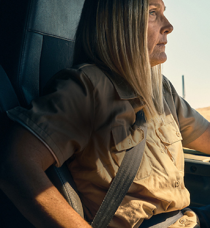 A woman inside the cab of a large vehicle driving on a road.