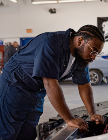 a man wearing dickies coveralls looking inside the front of a car