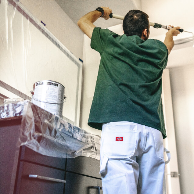 A painter using a tool to paint a ceiling.