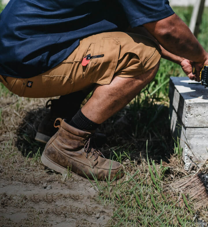 A person squatting while using an electric tool while wearing khaki-colored shorts