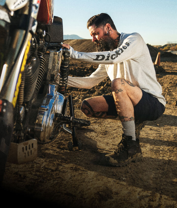 A person working on a two wheeled vehicle in a sunny outdoor setting.
