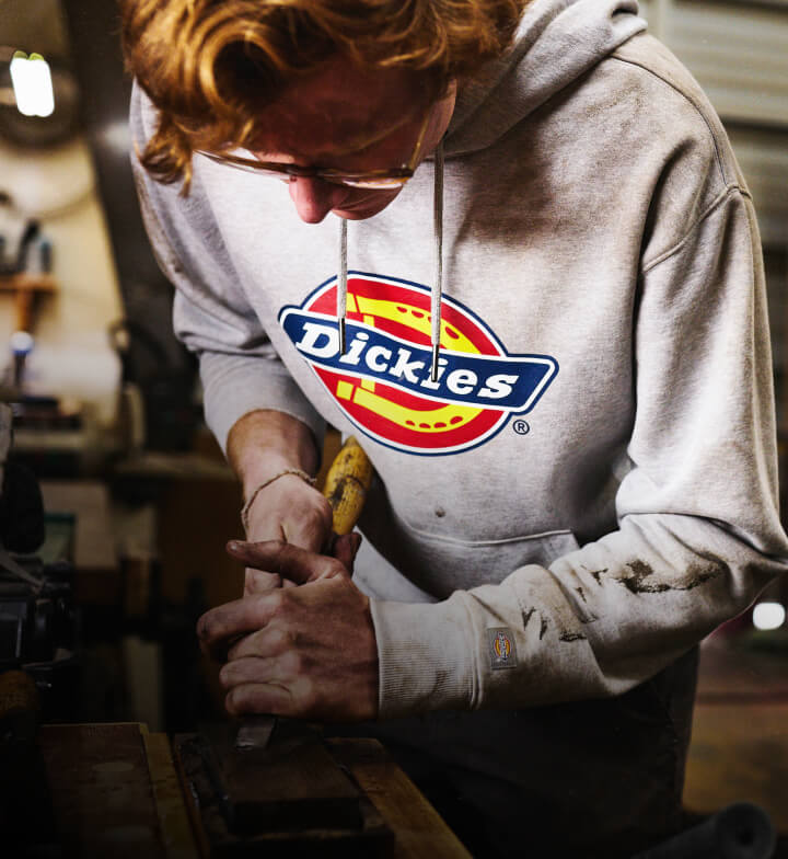 A man using a grinding type of tool wearing a white hoodie with a colored dickies logo.