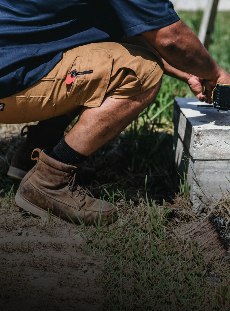 A worker wearing khaki-colored pants squatting while using a drill.