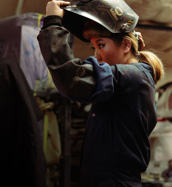 A worker holding a welding mask on their head.