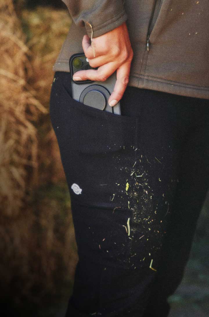 A person putting their phone into the pocket of their black utility pants.
