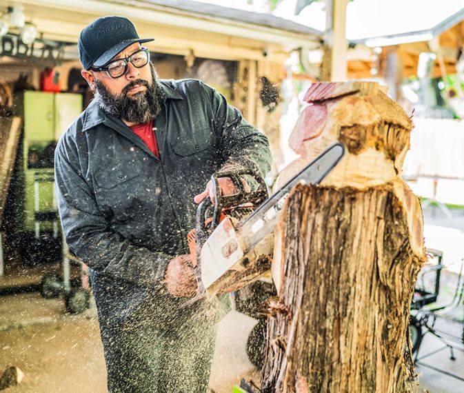 A worker using a chainsaw on a wooden log.