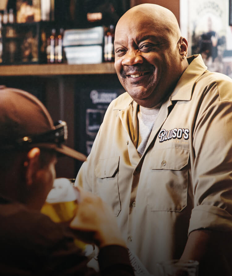 Kevin Bludso, owner of Bludso's BBQ smiling at two patrons in a bar setting.